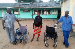 Three people stand outside Phumula Mission Hospital with wheelchairs.